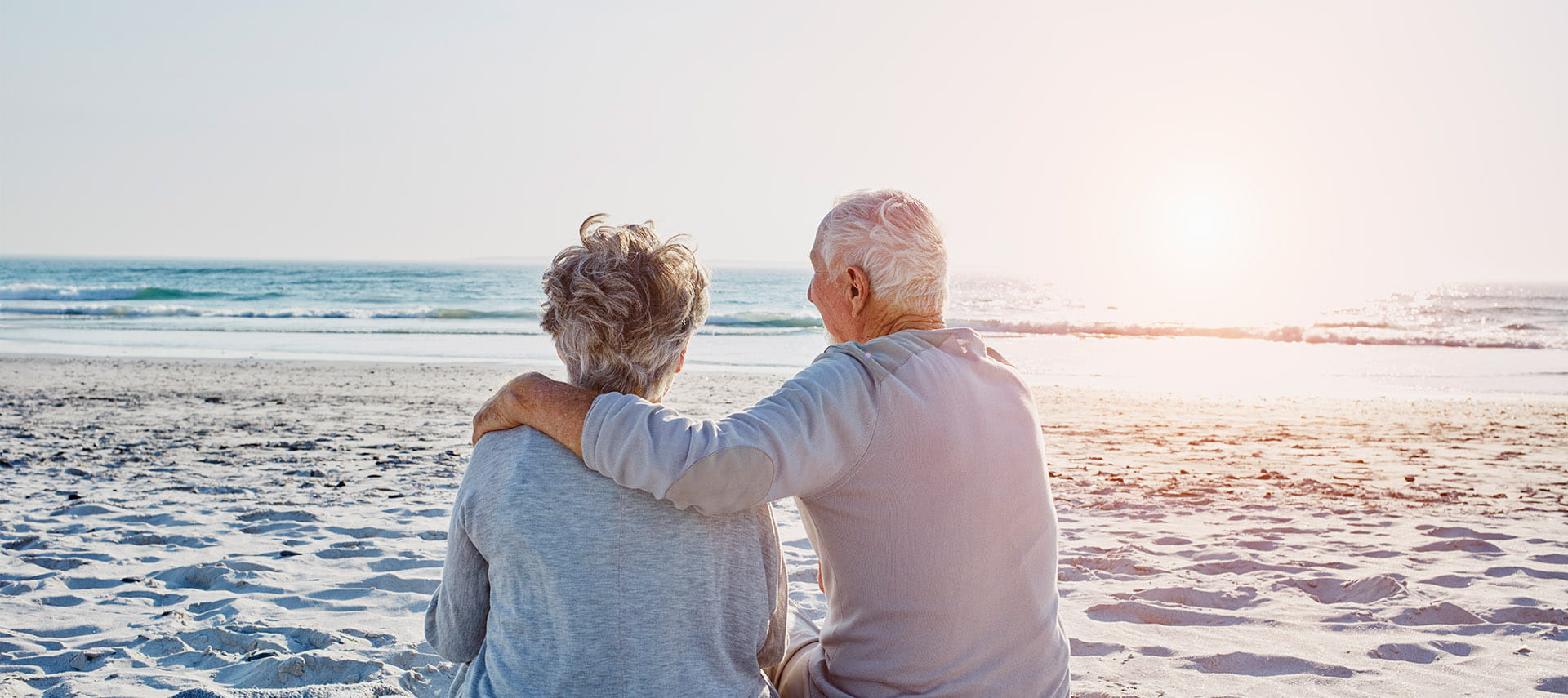 Mature couple sitting on the beach watching the sun set.